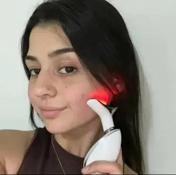 Woman using LED light therapy facial device on cheek for skincare