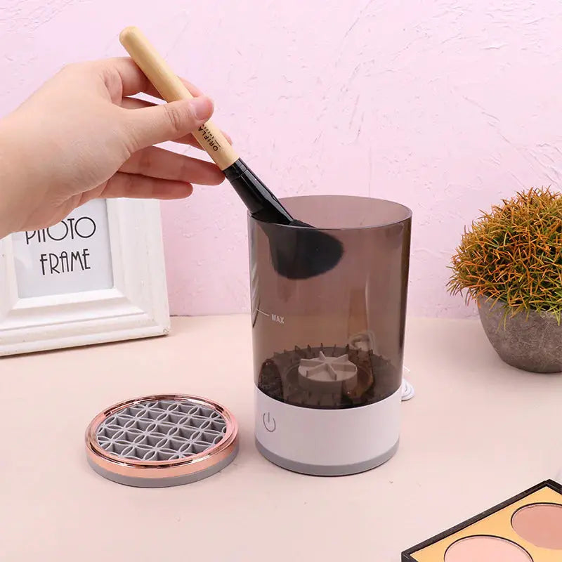 Electric makeup brush cleaner with hand holding brush above cleaning machine on vanity table